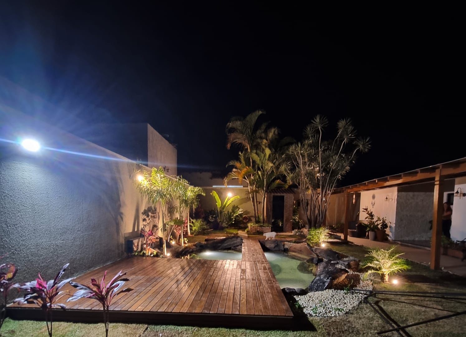 Jardim ornamental noturno com lago, deck e palmeiras iluminadas